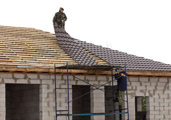 Workers install tiles on the roof of a house in winter - 792415966