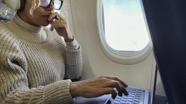 One adult woman travel on airplane on board using laptop computer sitting on the seat near thw window. Traveler on aircraft. Flight business online with computer. Modern traveler working and fly