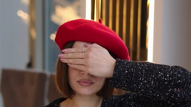 girl woman in red beret is covering eyes with hand palm and eating a dessert.female doesn't want to see what is eating.restaurant atmosphere.french cuisine