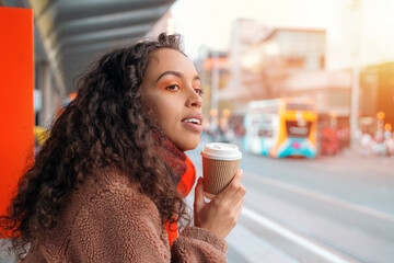 A cheerful woman holding a cup of coffee. A smiling curly brunette lady in a sweater waiting for a...