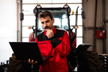 Serviceman with diagnostic tool standing by tractor machine and searching for a problem solution.