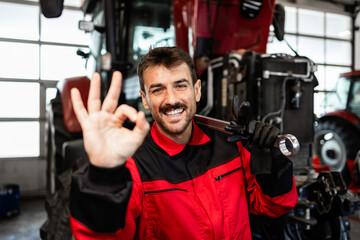 Mechanic standing in front of the tractor and showing okay gesture sign. Service and maintenance of agricultural machinery.