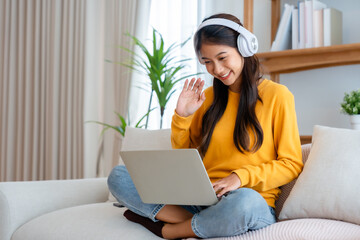 Young adorable asian woman smile wearing headset working in living room at home. Happy gorgeous female using computer laptop and sitting on couch at house, Video call with friend