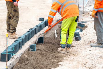Groundworker in orange hi-viz levelling semi-dry concrete and laying kerbs on new road construction