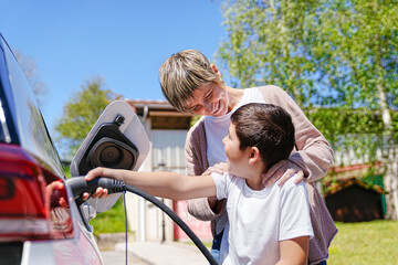 Mother shares a happy moment with son while connecting EV charger. - obrazy, fototapety, plakaty