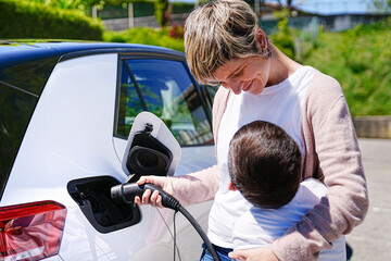Smiling mom and child connecting charger to electric car in daylight.