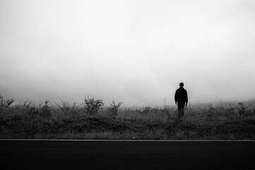 a man alone on the side of the road in foggy weather, looking sad and small