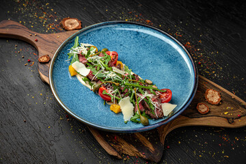 Warm salad of beef tenderloin, parmesan, vegetables and dressing. Menu for a pub on a dark...