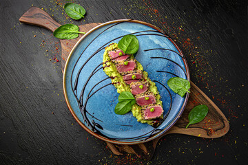 Tuna on a bed of avocado. Menu for a pub on a dark background. Colorful juicy food photography.