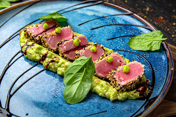 Tuna on a bed of avocado. Menu for a pub on a dark background. Colorful juicy food photography.