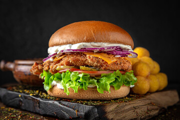 Gourmet chicken burger with cheese and veggies. Juicy delicious hamburger on darkmood picture for restaurant decoration, poster. 
