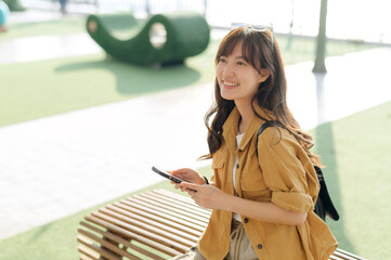 young Asian woman in 30s, phone in hand, explores a public platform. This portrait embodies the spirit of connected solo travel and cultural discovery. - 792476535