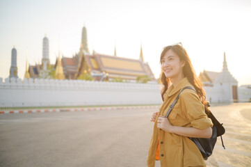 Traveler asian woman in her 30s, backpack slung over her shoulder, explores the intricate details of Wat Pra Kaew with childlike wonder. Sunlight dances on the golden rooftops. - 792478109