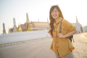 Traveler asian woman in her 30s, backpack slung over her shoulder, explores the intricate details of Wat Pra Kaew with childlike wonder. Sunlight dances on the golden rooftops. - 792478122