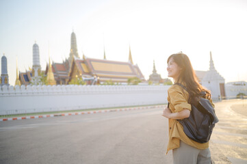 Traveler asian woman in her 30s, backpack slung over her shoulder, explores the intricate details of Wat Pra Kaew with childlike wonder. Sunlight dances on the golden rooftops. - 792478157