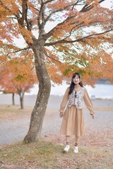 Asian woman in casual dress embraces the fall beauty of Japan, enjoying a holiday filled with smiles, fashion, and vibrant foliage. A cheerful portrait capturing the essence of a vacation.