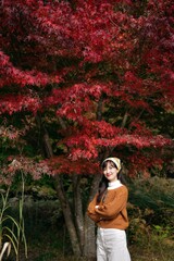 Asian woman, adorned in a stylish sweater, embraces the vibrant fall. A pretty and cheerful portrait capturing the essence of nature's colorful charm.