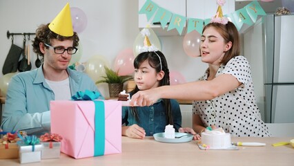 Caucasian mom cutting birthday cake and separated dessert while give to father. Happy family wear party hat to celebrated daughter birthday while sitting at table. Special occasion concept. Pedagogy.