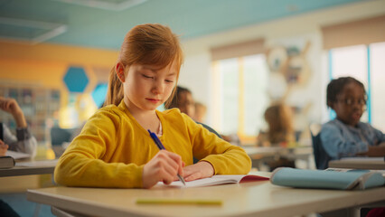 Portrait of a Cute Smiling Girl with Bright Ginger Hair Sitting Behind a Desk in Class in...