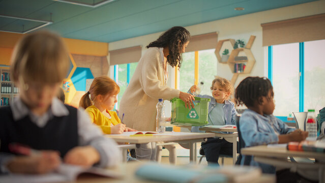 Elementary School Classroom: Enthusiastic Female Teacher Gathering Empty Plastic Bottles in a Box with a Recycling Label and Explaining Ecology and Sustainability Concepts to School Kids