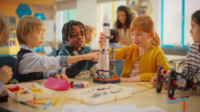 Elementary School Students Sitting Behind a Table in a Group, Building a Space Rocket Model for a Science and Technology Fair. Young Boys and Girls Wish to Become Engineers and Space Explorers