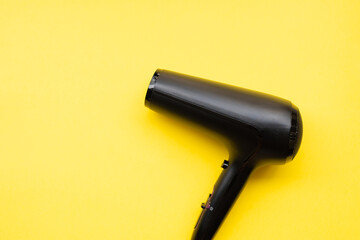 Black hair dryer on blue and yellow paper background.