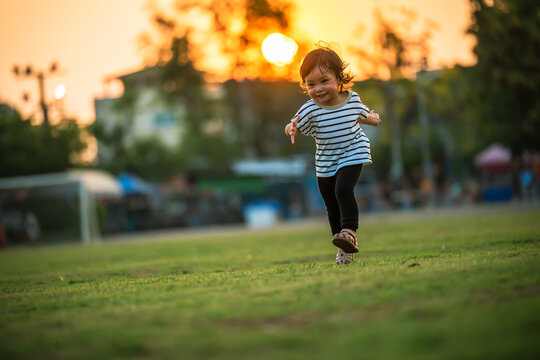 happy toddler girl running on grass field in park at sunset