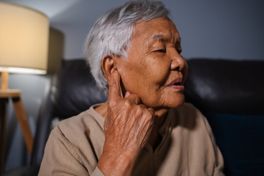 senior woman with symptom of hearing loss while sitting on sofa in the living room at night
