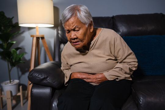 senior woman suffering from stomach ache  while sitting on sofa in the living room at night