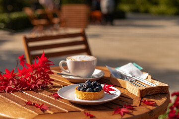 Cozy Autumn Cafe: Cappuccino & Blueberry Tart Outdoors with Vibrant Fall Foliage.