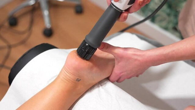 Close-up of an unrecognizable patient on stretcher receiving a shockwave therapy massage on foot in a holistic clinic