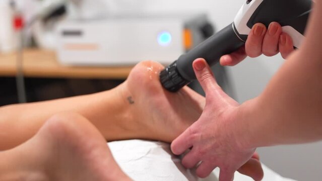 Unrecognizable patient undergoing modern therapy to reduce pain through shockwaves at a physiotherapy and massage clinic