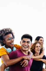 Vertical photo of diverse group of young people having fun together outdoors. Happy multiracial men giving girlfriends piggyback ride. Friendship lifestyle concept.