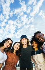 Vertical portrait of young group of happy multiracial people standing outdoors over blue sky....