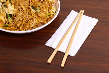 Fried noodle with chicken and vegetables in a white bowl on a wooden table. After edits.