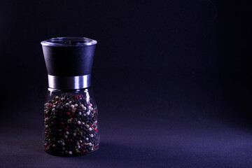 Fragrant multicolor peppercorns in a pepper shaker on a black background