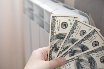 Dollars money banknotes are on heating radiator battery. Concept of expensive heating costs and...