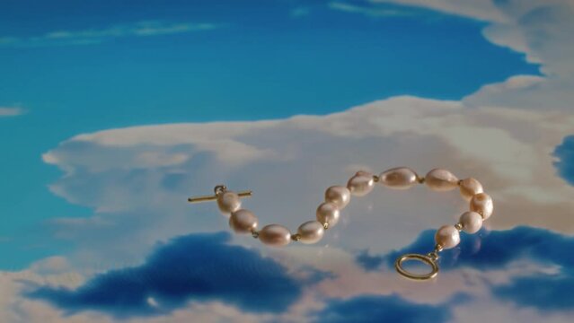 No people product shot of advertisement of gold bracelet with natural pearls lying on digital surface picturing bright blue sky with clouds