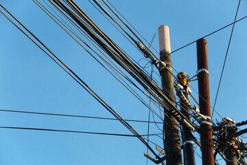 Power poles and chaotic power lines against a background of bright blue sky in the morning. suitable for industrial and electrical themes.