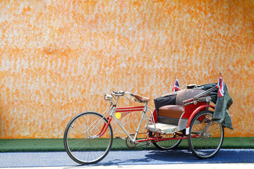 An old tricycle stops as a check-in point at a restaurant with an orange cement wall background. In the past, it was a vehicle that Thai people preferred to use. Currently serving tourists.