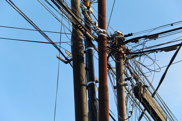 Power poles and chaotic power lines against a background of bright blue sky in the morning. suitable for industrial and electrical themes.