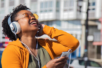young black woman with headphones and phone on the street enjoying free