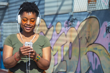 young african american woman with headphones and phone with graffiti wall background