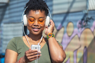 young woman with headphones and phone with graffiti wall background