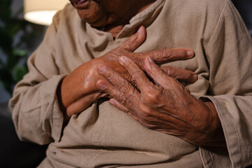 close up senior woman suffering from bad pain in her chest heart while sitting on sofa in the living room at night