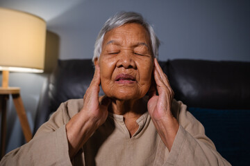 senior woman with symptom of hearing loss while sitting on sofa in the living room at night