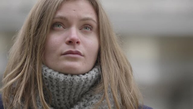 A young blonde woman with long hair stands wrapped in a scarf, her expression tinged with sadness amidst the crisp autumn air