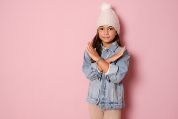Brunette kid girl in knitted hat over pink background Has rejection angry expression on face and...