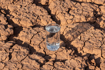 A glass of clean water stands on heat-cracked clay in the desert