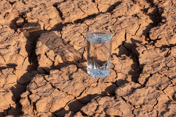 A glass of clean water stands on heat-cracked clay in the desert